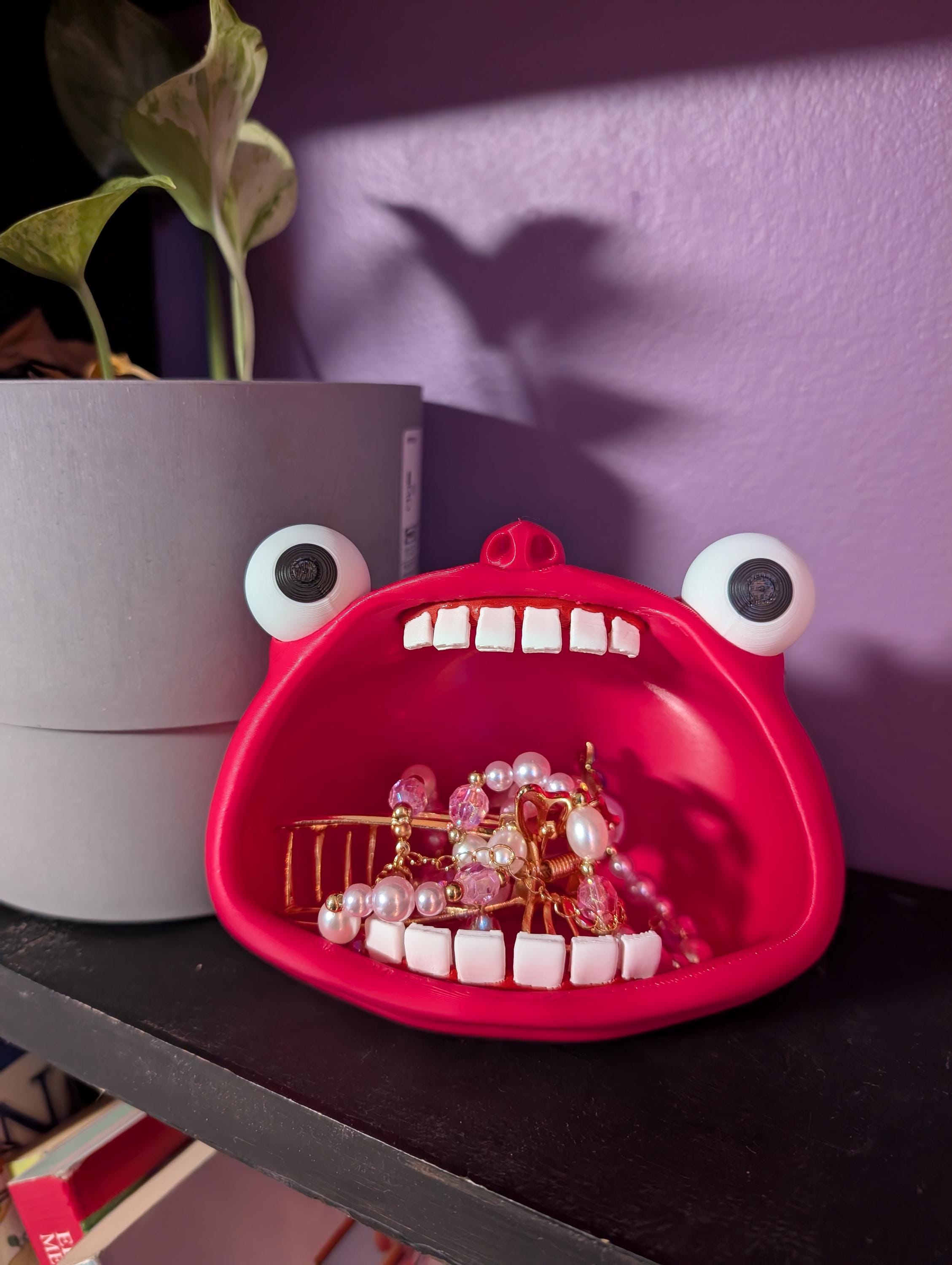 A wide-eyed monster with his mouth wide open, shown holding some jewelry in its mouth.