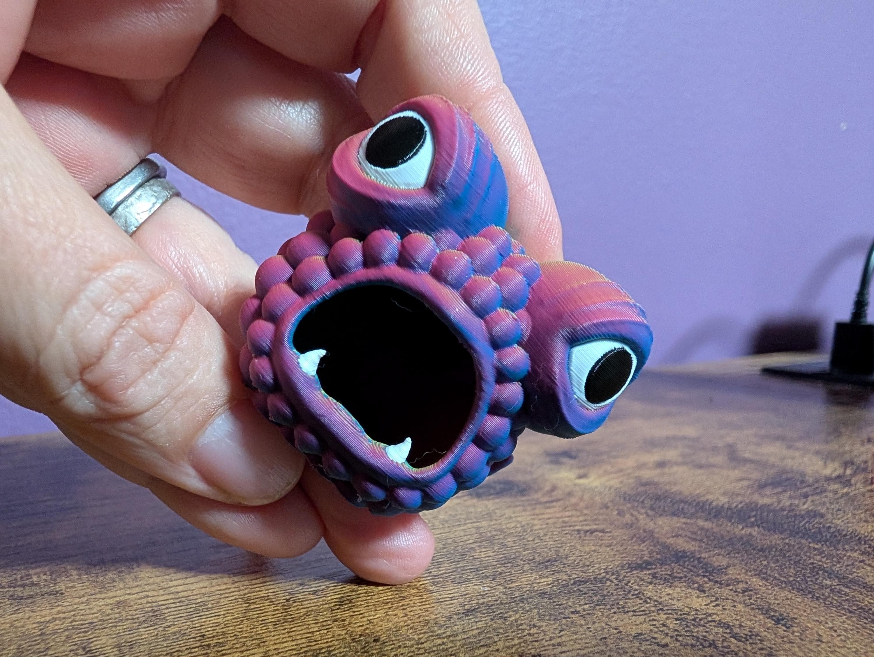 A wide-mouthed, wide-eyed fish trinket being held in a hand.