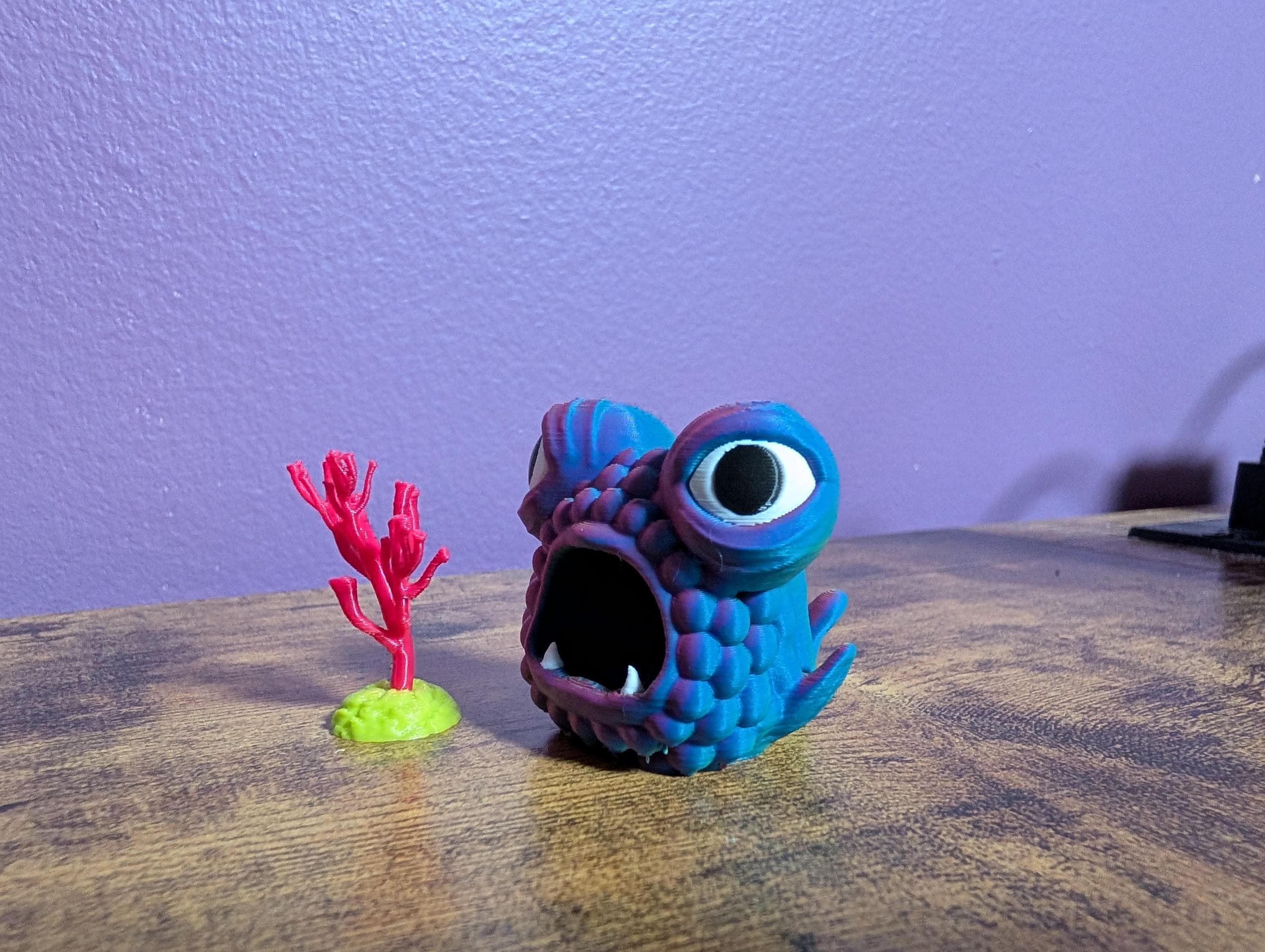 Side view of a 'tri-color' fish, the colors change based on the angle.  This is a trinket sided desk companion or shelf buddy. Shown beside a piece of tiny coral.