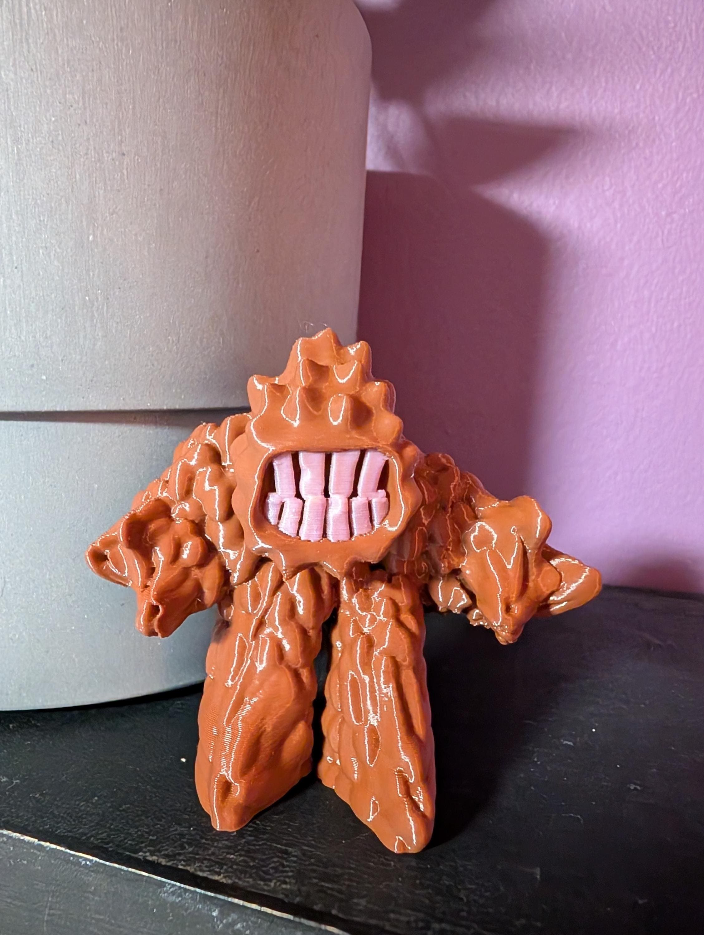 Mini Mud Monster figurine with big teeth and bumpy body, cute but mischievous desk or shelf decor. Freestanding on a shelf with a purple background.