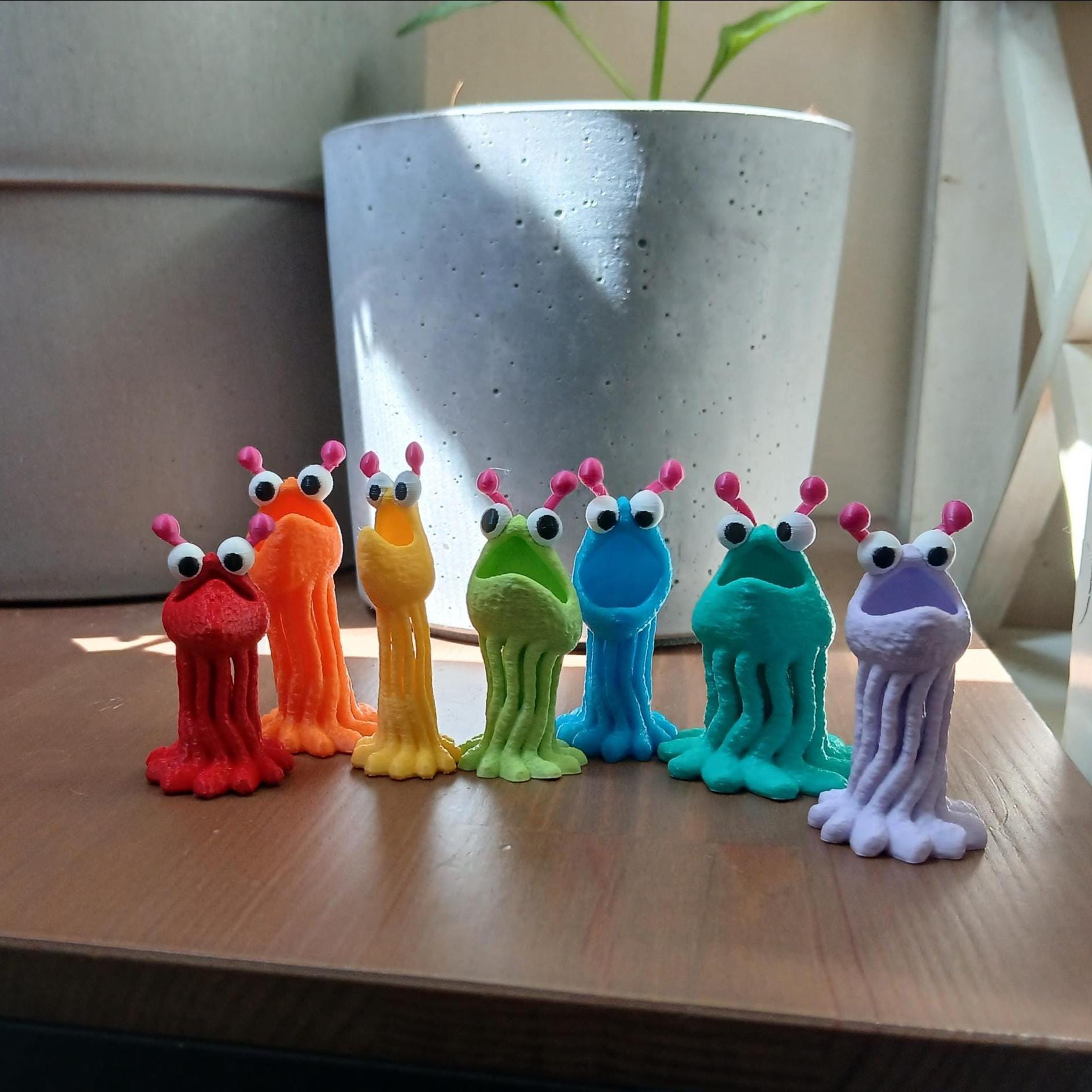 Colorful toy monsters on a wooden surface with a plant pot in the background