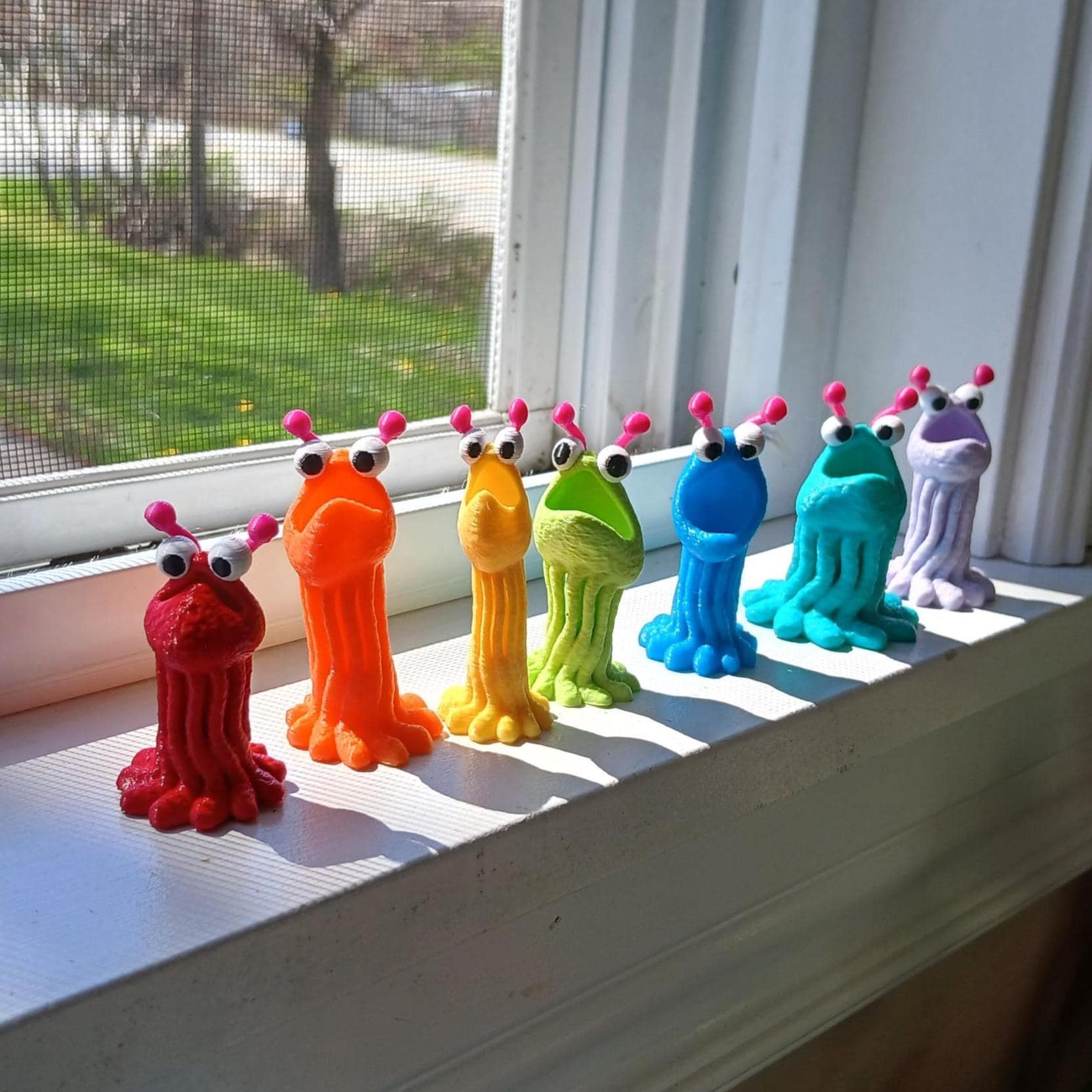 Colorful martian figurines on a windowsill with a view of greenery outside.