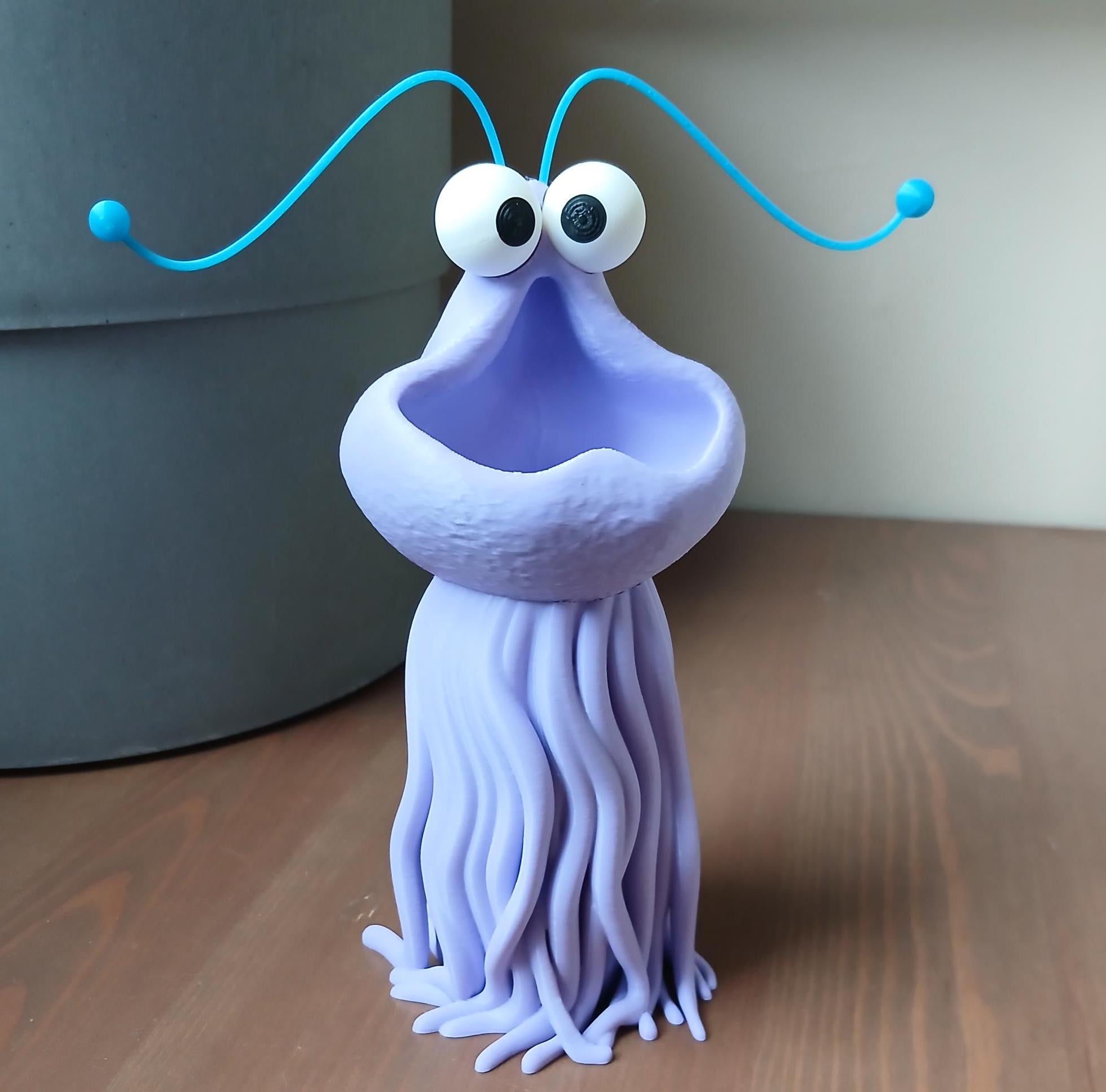 Purple alien-like creature figurine with blue antennas on a wooden surface
