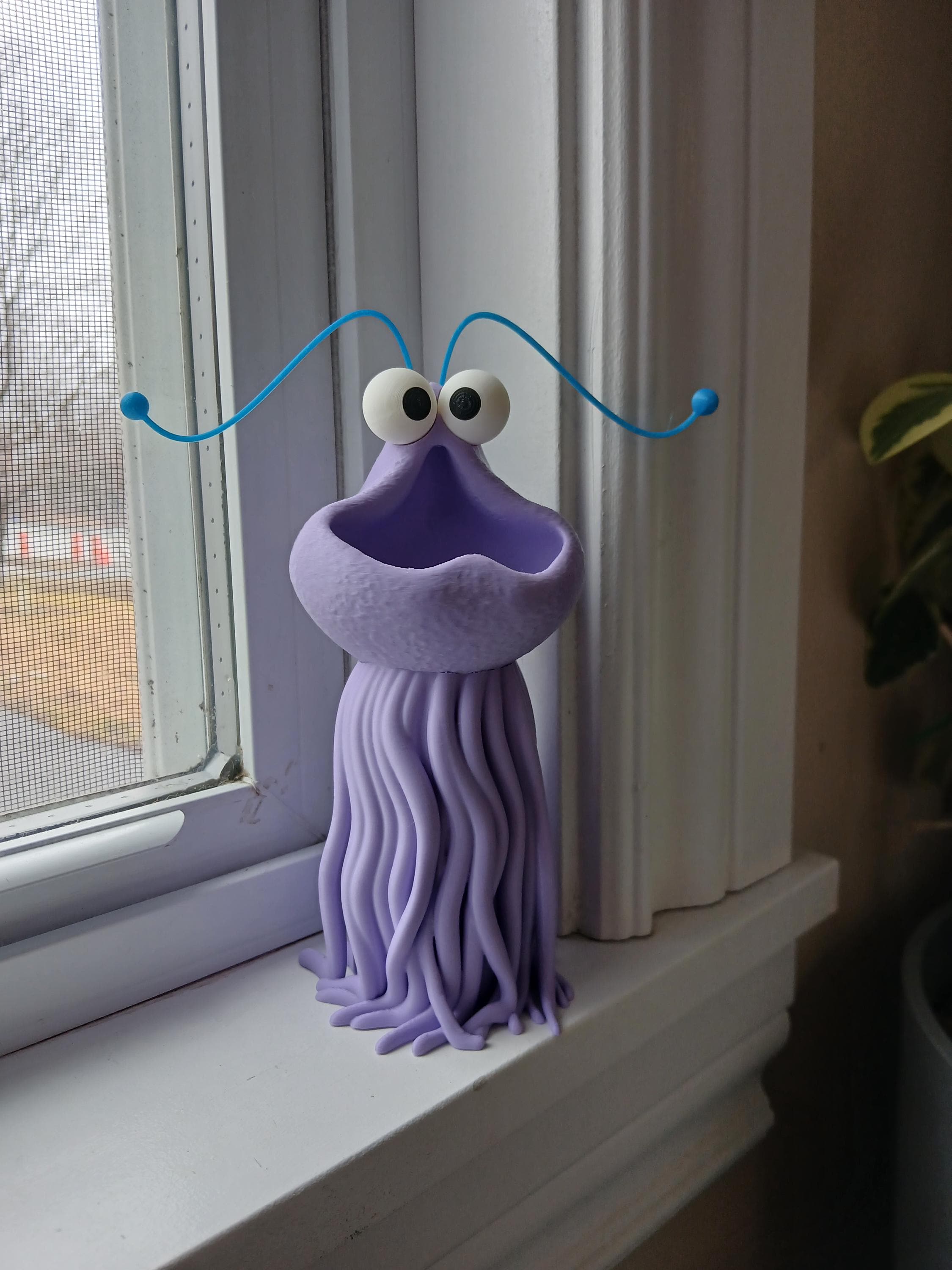 Purple creature figurine with blue antennas on a windowsill