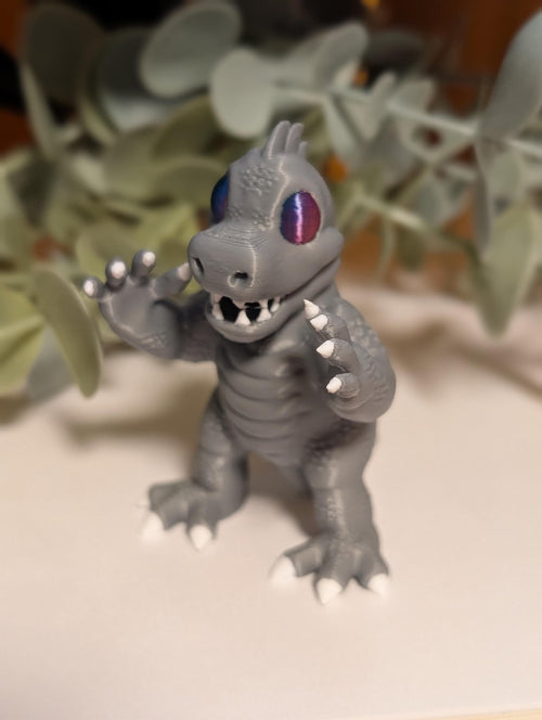 cute 3D printed mini monster figurine with purple eyes standing on a book beside green plant leaves